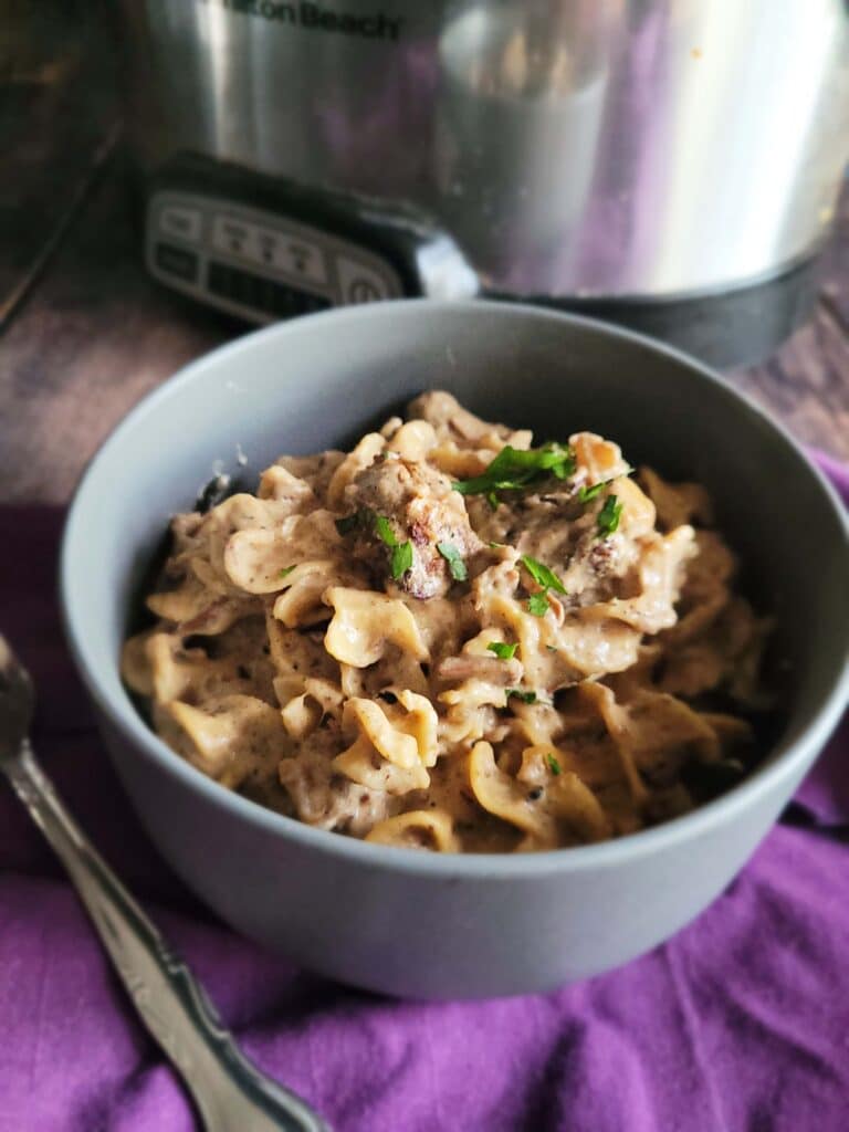 Creamy crockpot beef stroganoff served over egg noodles in a bowl