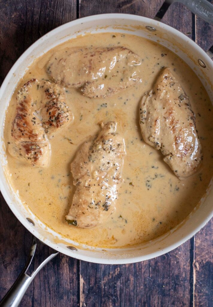 chicken simmering in a large pan of lemon garlic sauce