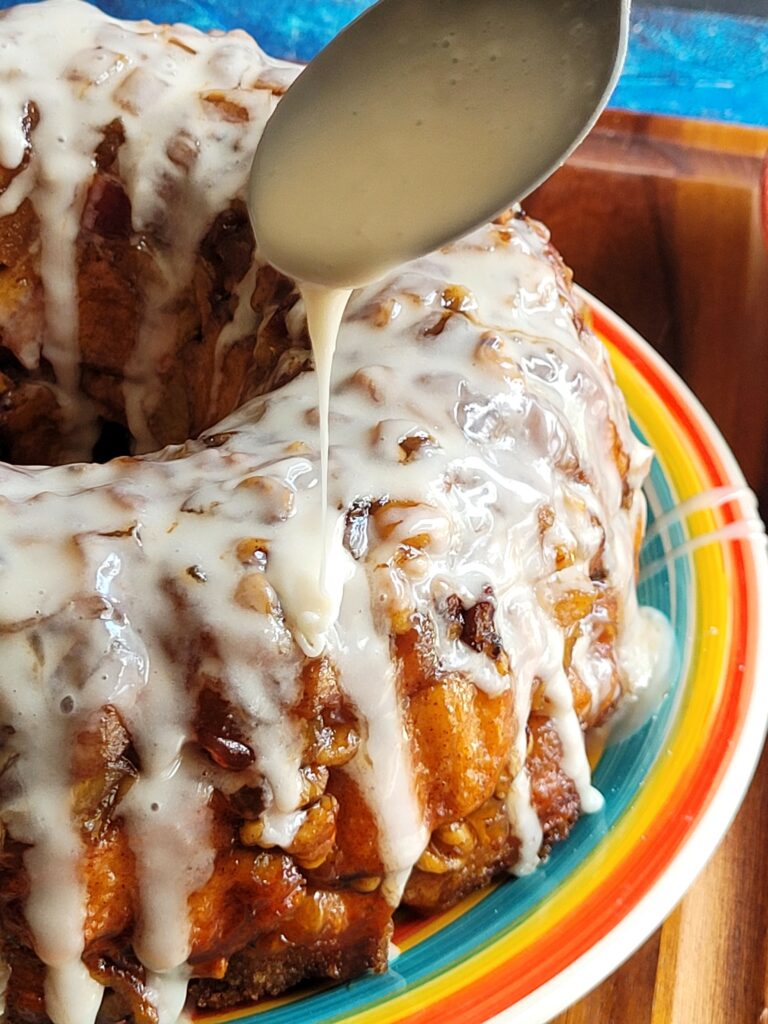 This Apple Fritter Monkey Bread is a gooey pull apart bread that is reminiscent of your favorite bakery apple fritters. Made withe refrigerated biscuit dough, this apple monkey bread is tender but with a crunchy crust, layered with apples, walnuts and cinnamon sugar then topped off with a vanilla icing drizzle sure to make this your favorite fall baking recipe!