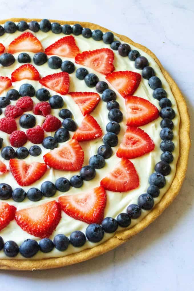 Red White and Blue Fruit Pizza is an easy fruit pizza that tastes amazing and will be your favorite Fourth of July dessert. Made with a Pillsbury sugar cookie crust, fresh fruit, powdered sugar, lime and cream cheese, this Red White and Blue Fruit Pizza is the perfect patriotic dessert to show off your Ameican pride! | A Wicked Whisk