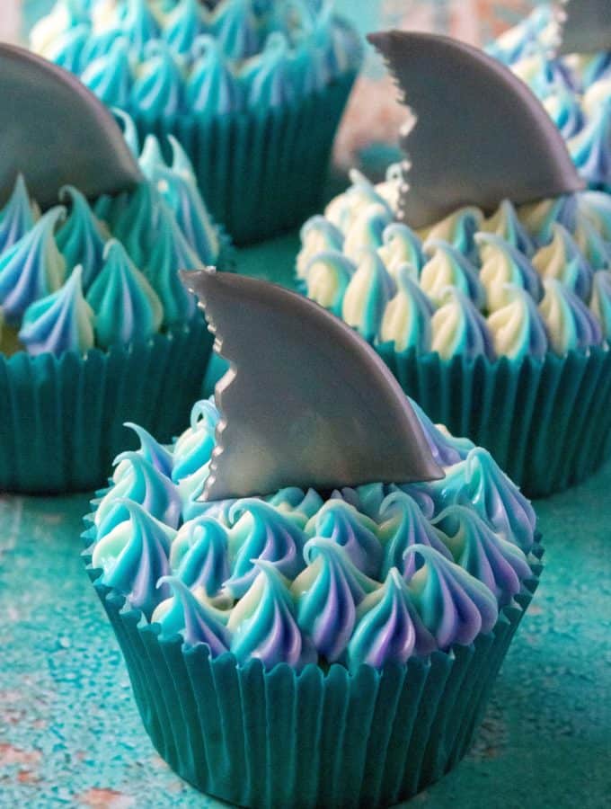Shark Week Cupcakes are easy to make, fun to eat and the perfect sweet treat to sink your teeth into. Homemade orange cupcakes filled with a bite of rasberry orange sauce, these Shark Week Cupcakes are great for viewing parties, days at the beach or watching your favorite shark show on TV.