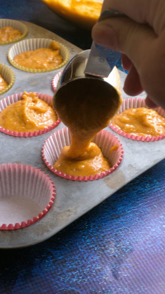 pouring pumpkin muffin batter into the muffin tin