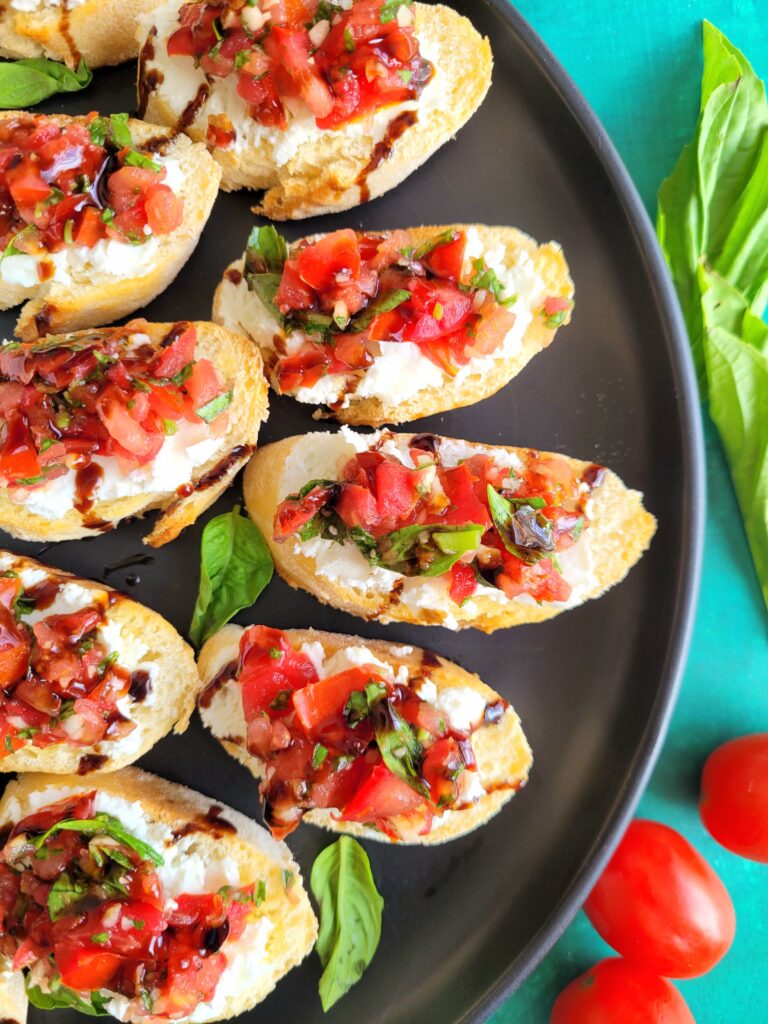 Tomato goat cheese bruschetta on toasted baguette slices, drizzled with balsamic glaze and garnished with fresh basil on a serving platter