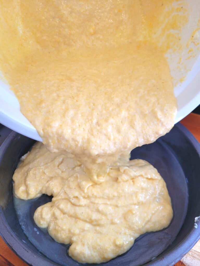 pouring jiffy cornbread batter into hot metal baking pan