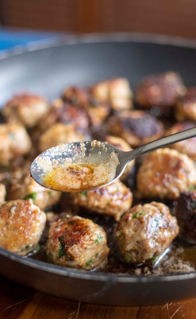 cooking italian herb meatballs in a skillet