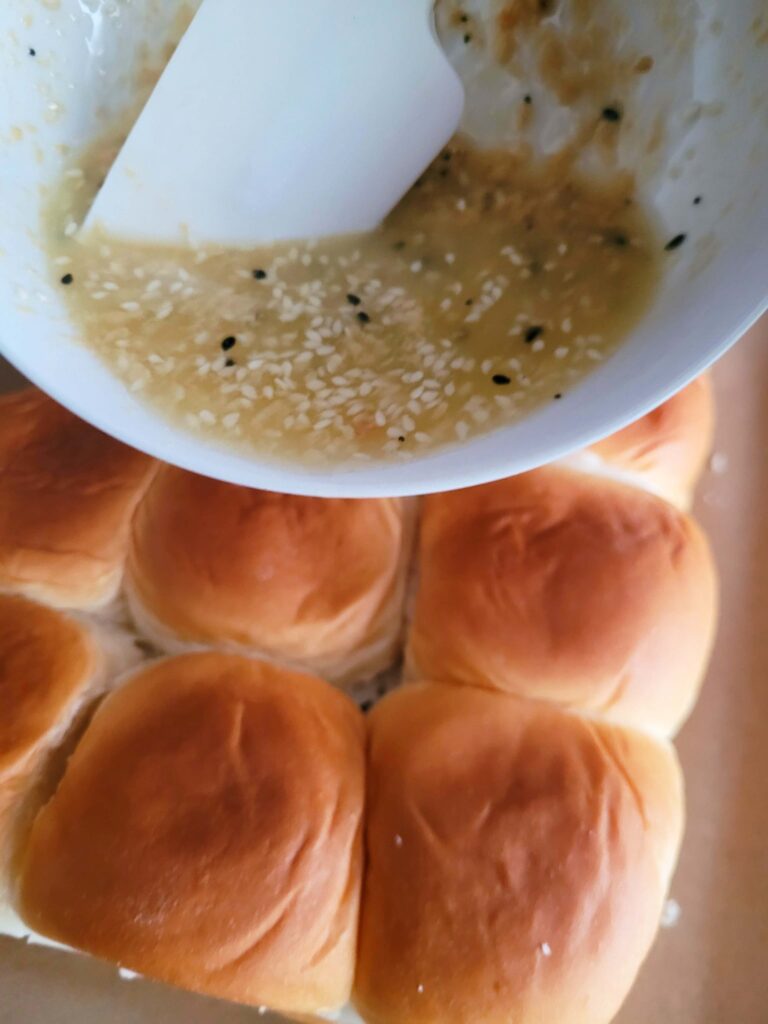 pouring seasoned butter over ham and cheese game day sliders
