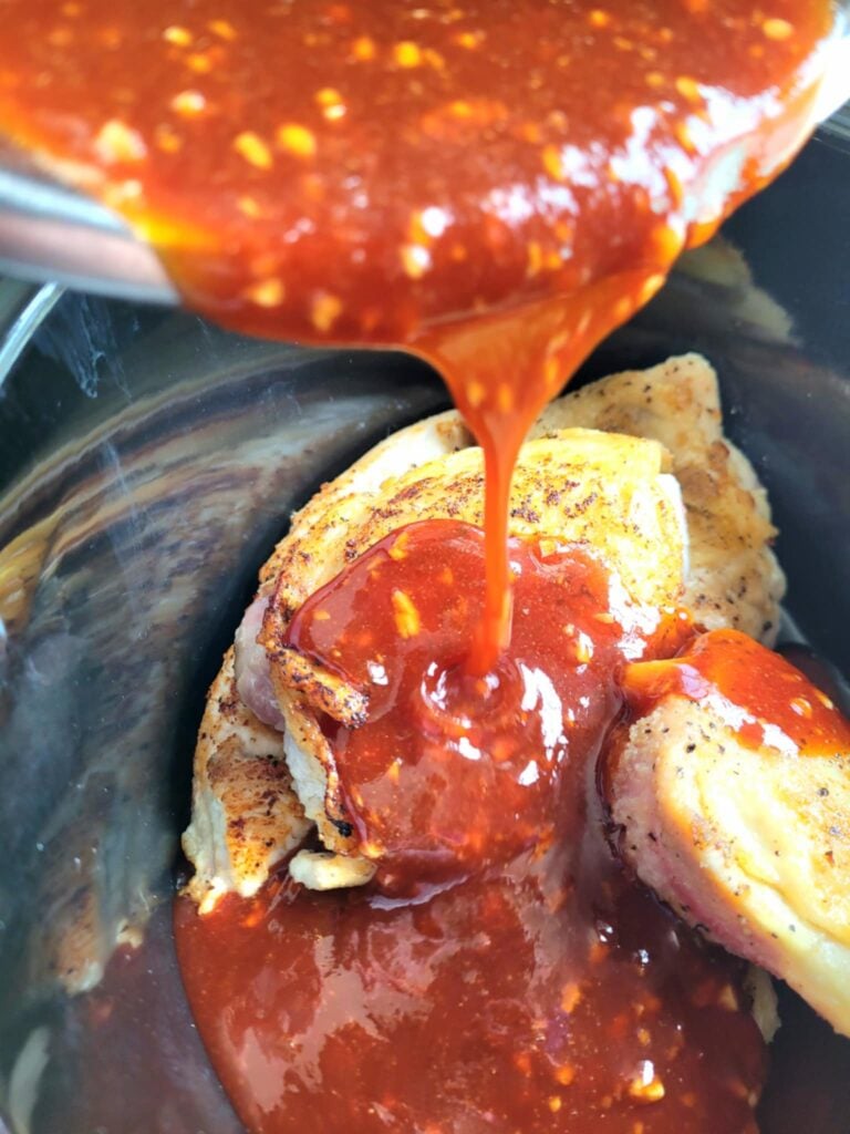 pouring asian inspired sauce over chicken in slow cooker
