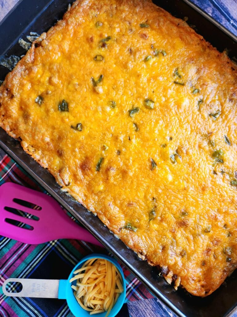 tater tot breakfast casserole with melted cheddar, crumbled sausage, crispy bacon, and green onion garnish in a 9x13-inch baking dish.