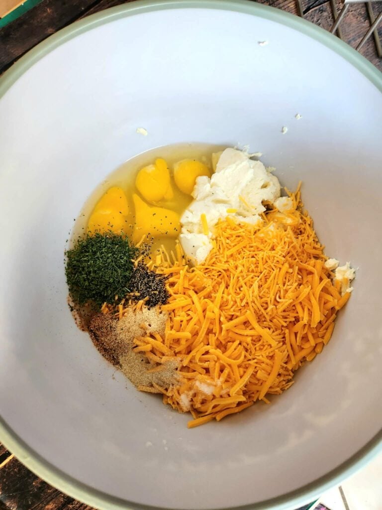 Whisking eggs, ricotta, shredded cheddar, sausage mixture, parsley, and seasonings in a large bowl.