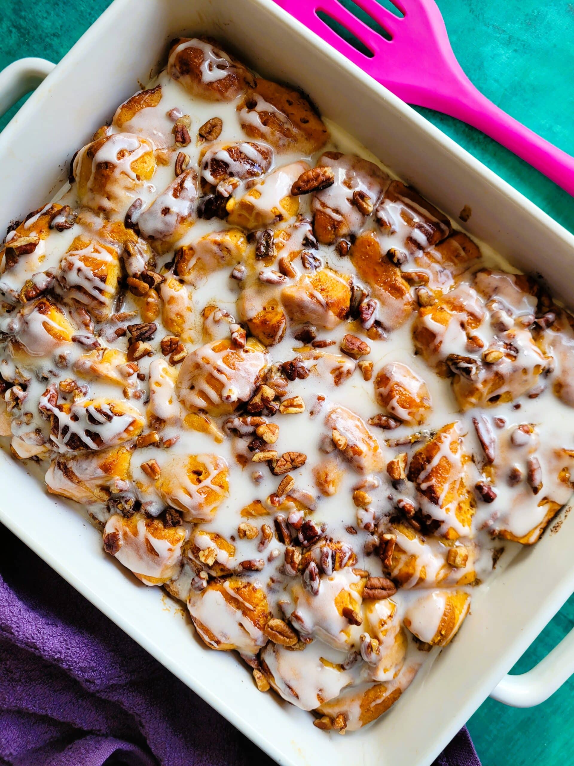 Overhead shot of the baked cinnamon roll breakfast casserole, maple syrup and icing drizzled, ready for serving at a holiday brunch table.