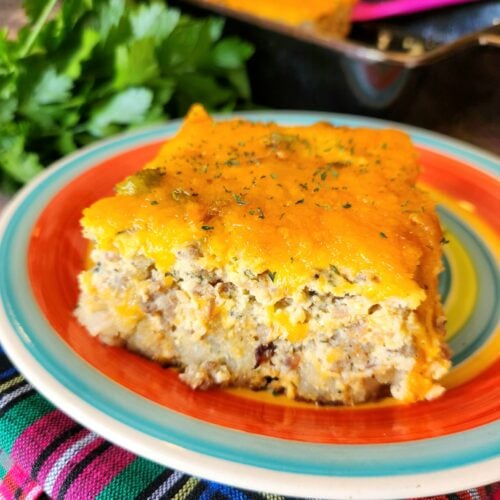 Cheesy tater tot breakfast casserole with melted cheddar, crumbled sausage, crispy bacon, and green onion garnish in a 9x13-inch baking dish.