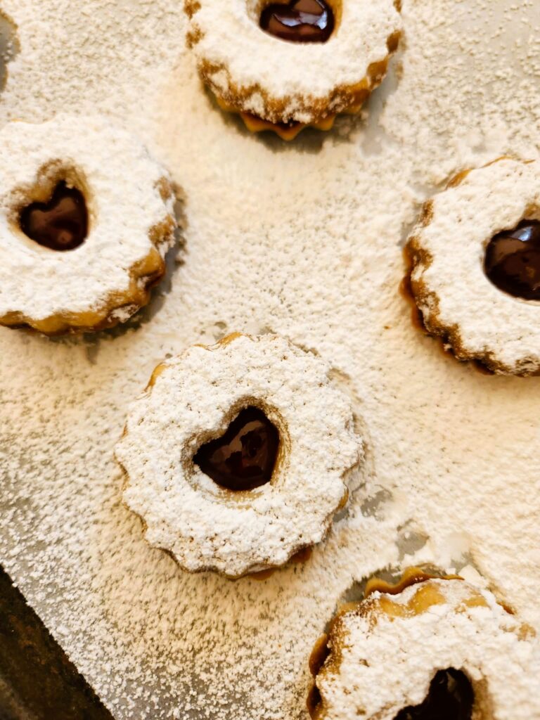 Single raspberry jam cut-out cookie on parchment with jam peek-through.