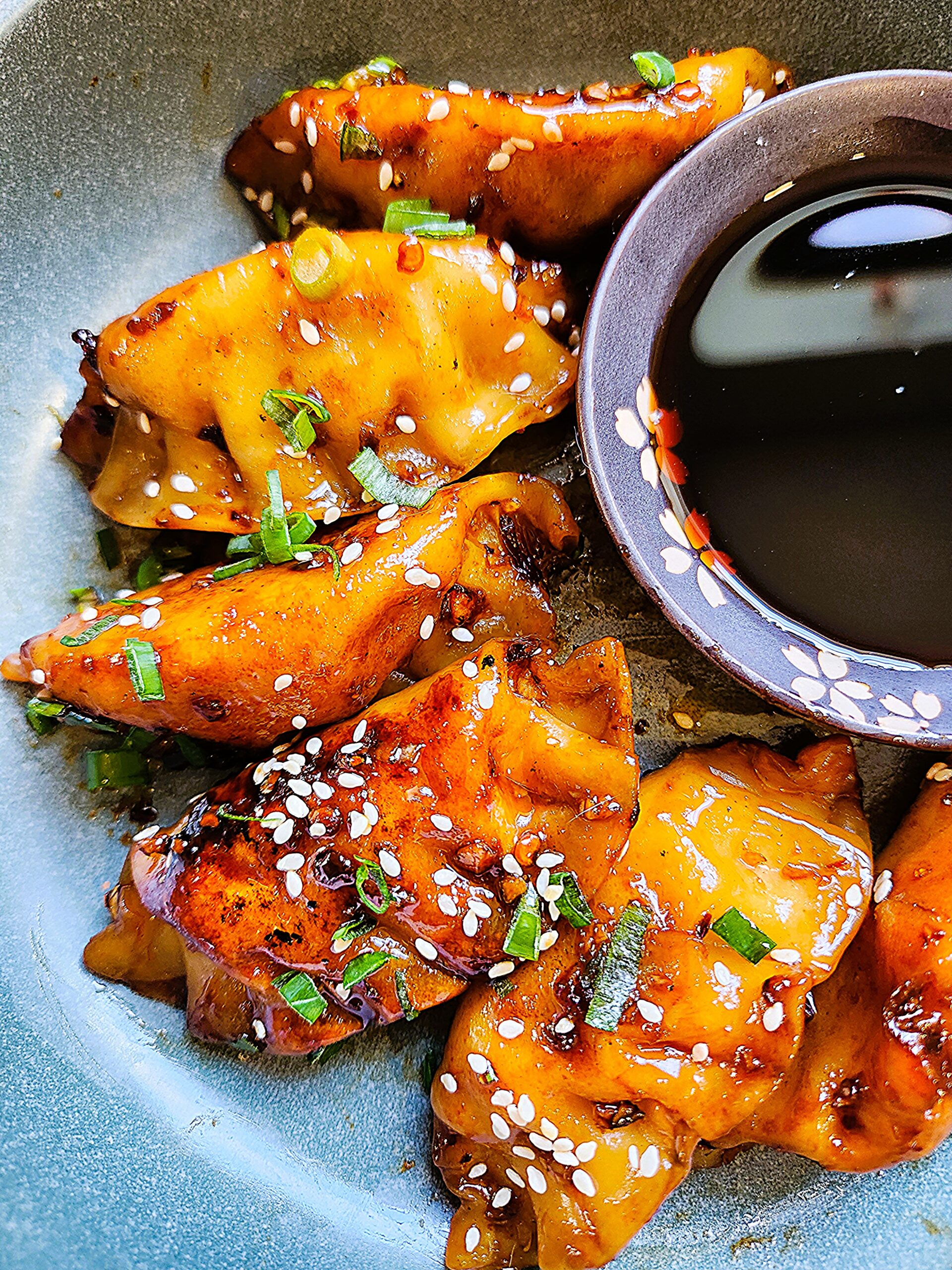 Golden-brown crispy honey soy pork potstickers on a plate, garnished with sesame seeds, sliced scallions, and red pepper flakes.