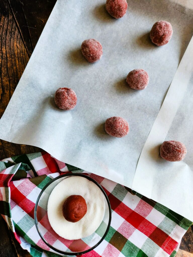 Scooping red velvet cookie dough balls onto a parchment-lined baking sheet – ready for baking thick, soft red cookies.