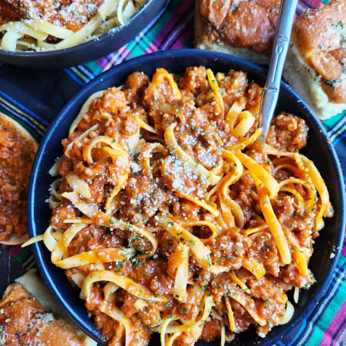 Bowl of rich beef bolognese sauce over fettuccine with grated Parmesan
