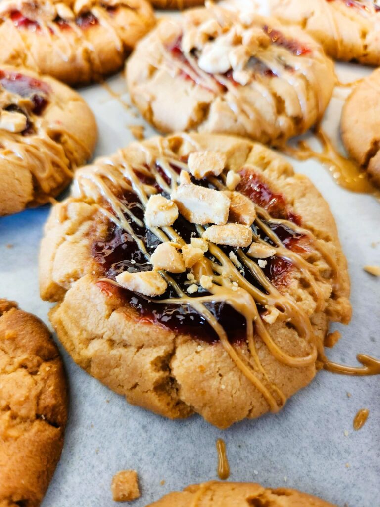 Soft peanut butter and jelly cookies with jam centers and peanut drizzle. Classic PB&J thumbprint cookies and nostalgic peanut butter dessert.