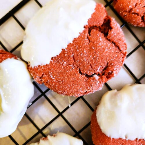 Close-up of chewy red velvet cookies with sugar-crackled edges and creamy white chocolate dip.