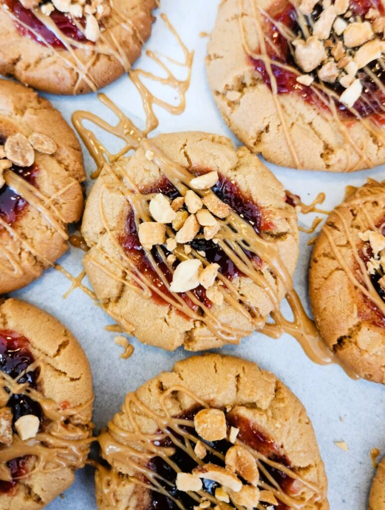 Close-up of PB&J thumbprint cookies showing glossy jam center and peanut butter drizzle