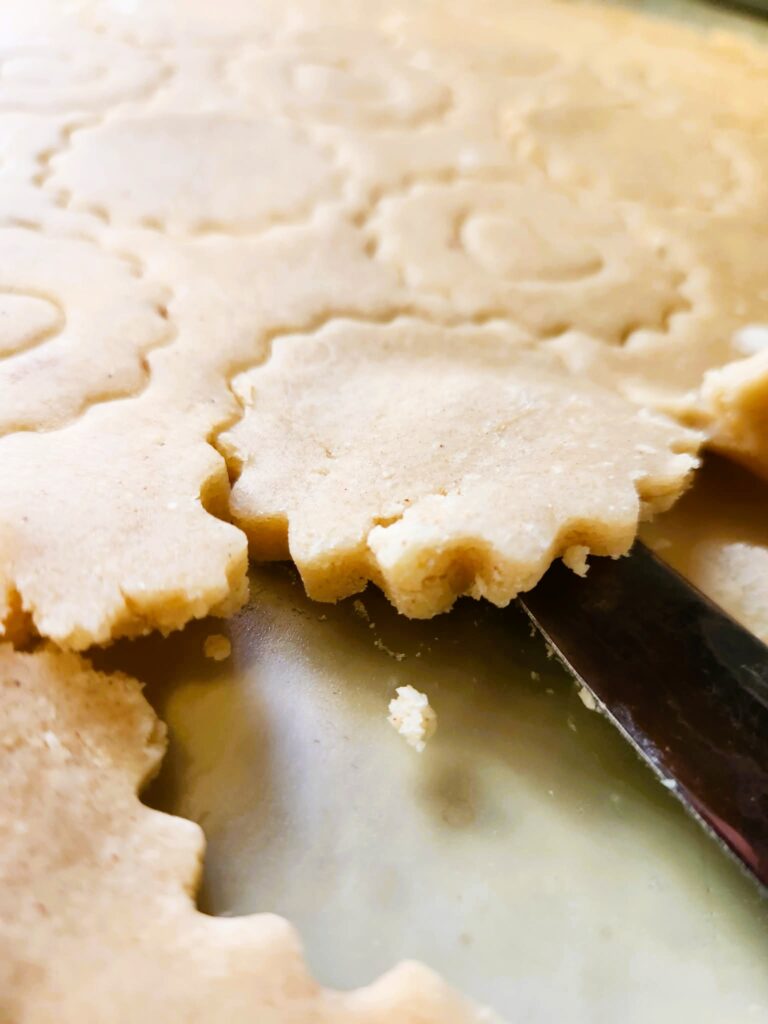 Lifting cut-out cookies from the board using a butter knife.