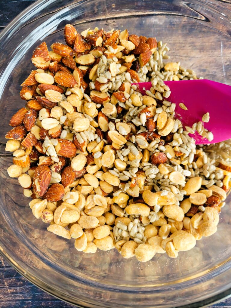 Mixing roasted almonds, peanuts, and sunflower seeds into syrup mixture for nut bars