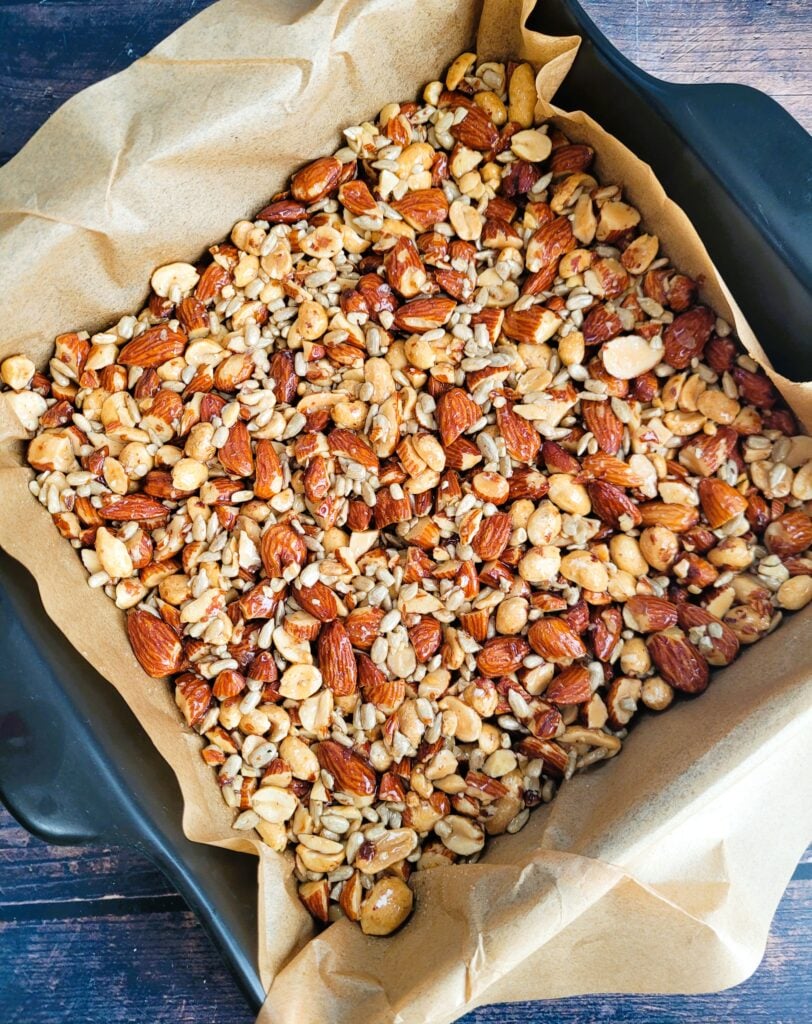 Pressing nut mixture firmly into parchment-lined pan for crunchy snack bars.