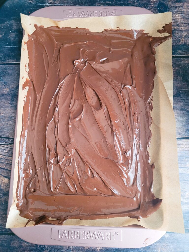 Spreading melted chocolate as the base layer in a parchment-lined pan.