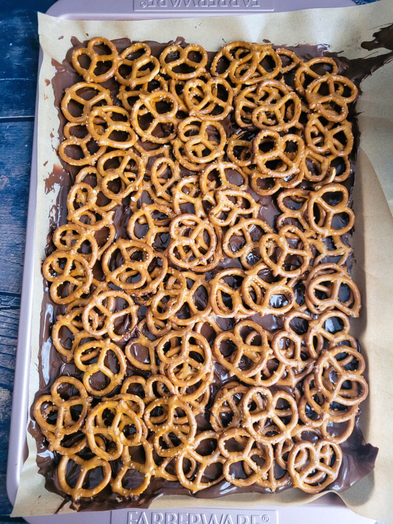 Sprinkling chopped pretzels evenly over the chocolate layer for easy layered candy bars at home