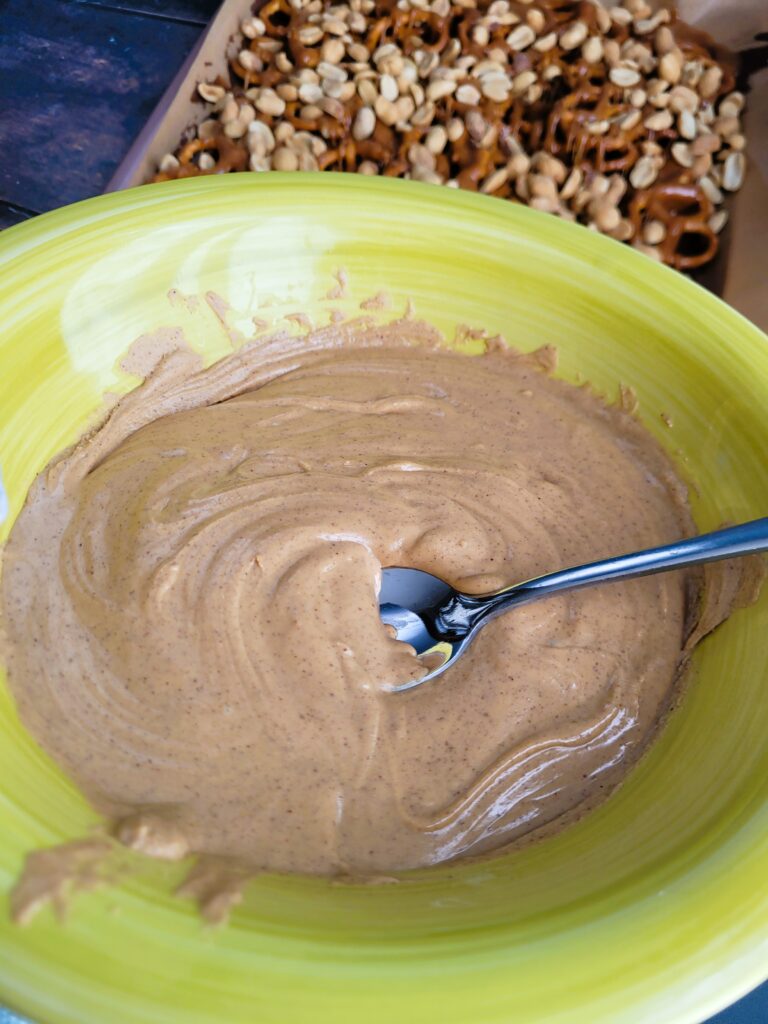 Drizzling melted peanut butter chips evenly over peanuts in DIY peanut butter chocolate caramel bars