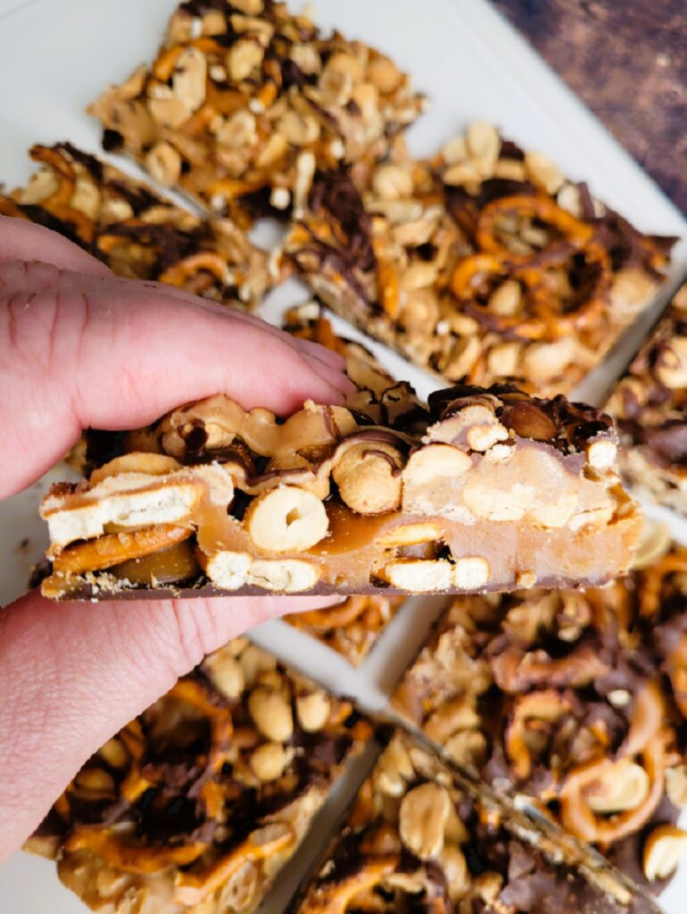 Close-up of one homemade Take 5 bar showing all five layers: chocolate, pretzels, caramel, peanuts, and peanut butter.