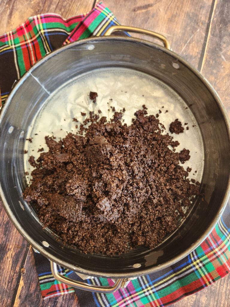 Chocolate cookie crust pressed into 9-inch springform pan with melted butter and espresso powder, ready for baking.