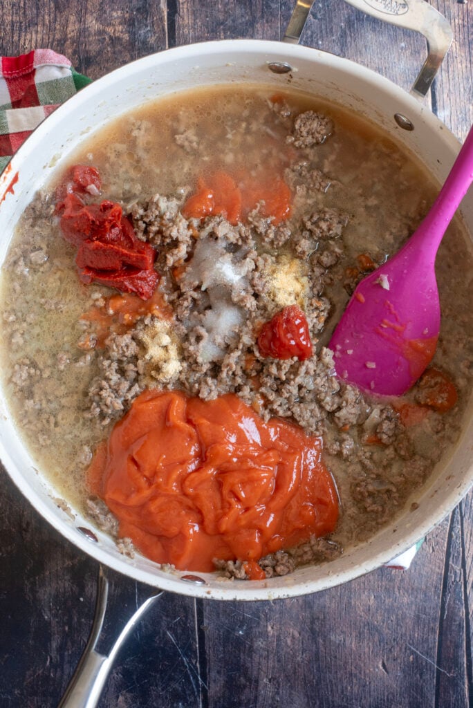 Adding 20โฏoz concentrated tomato soup, 2 cans water, 3 tablespoons tomato paste, 1 tablespoon ketchup, 1 tablespoon sugar, and seasonings to beef