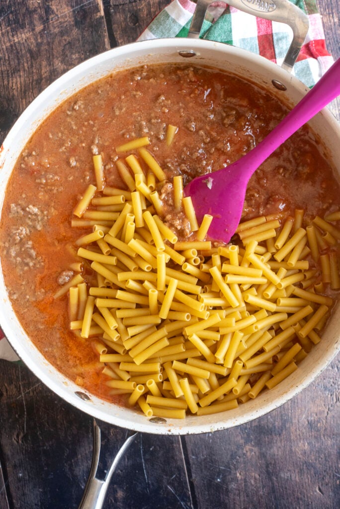 Stirring in 3 cups dry ziti pasta into simmering beefaroni sauce