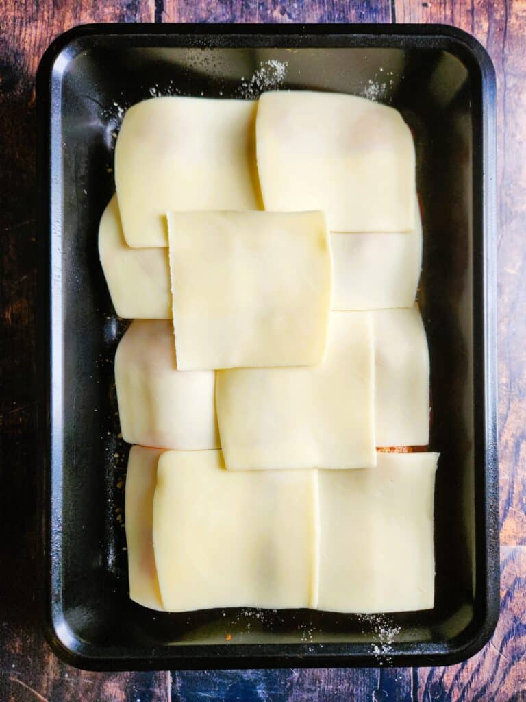 Mozzarella slices being placed over baked chicken meatballs in tomato sauce before melting