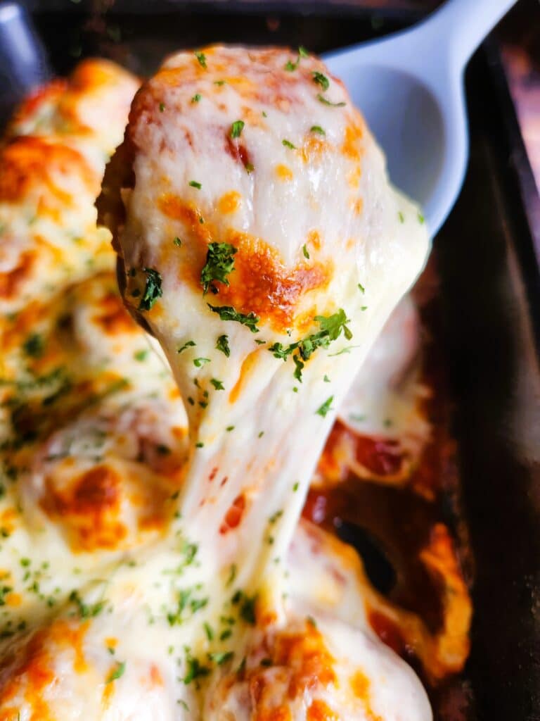 Close-up of juicy baked chicken meatballs coated in tomato sauce and melted mozzarella cheese with browned, bubbly top