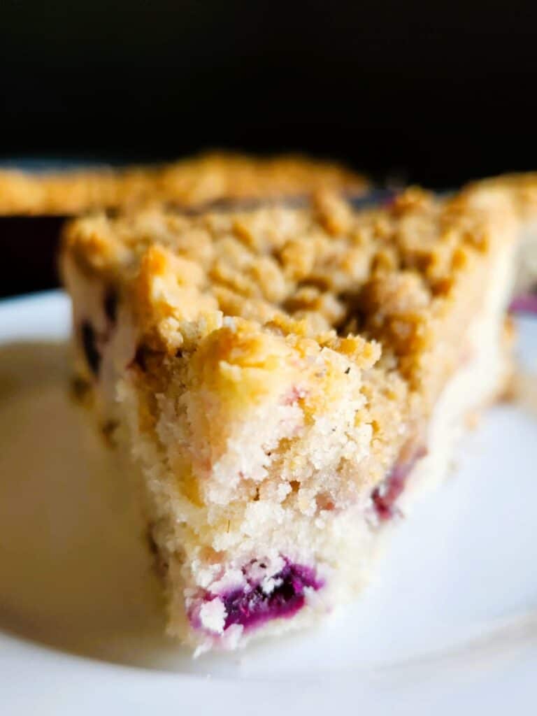 Slice of warm blueberry raspberry skillet cake with crumble topping showing soft cake layers and juicy berries inside.