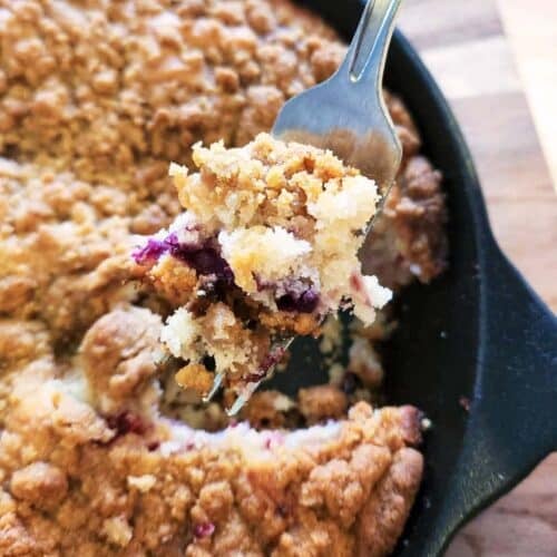 Close-up of baked berry skillet cake showing juicy blueberries, raspberries, and crisp golden crumble topping.