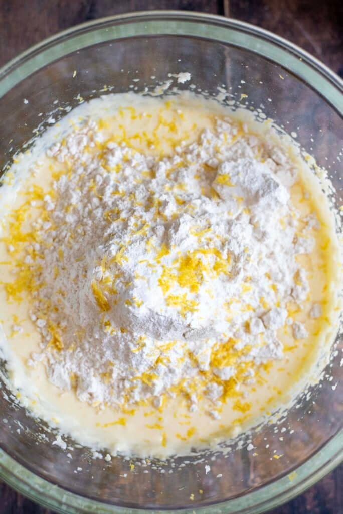 Lemon berry cake batter being mixed in a bowl with flour, sugar, sour cream, and lemon zest.