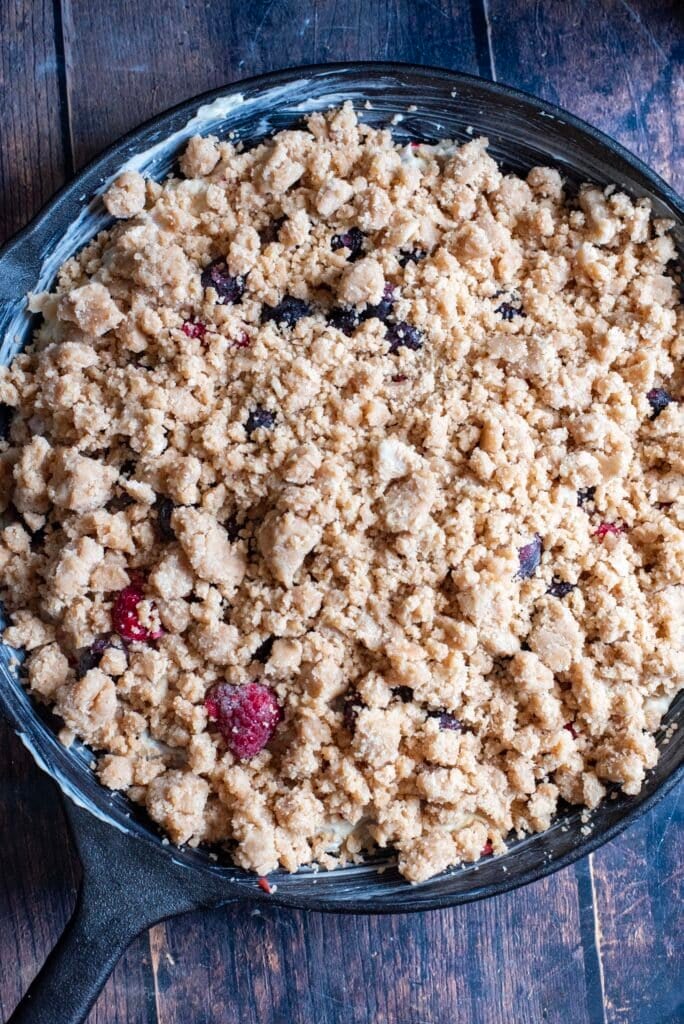 Golden baked lemon berry skillet cake with blueberry and raspberry filling topped with a buttery crumble crust in a cast iron skillet.