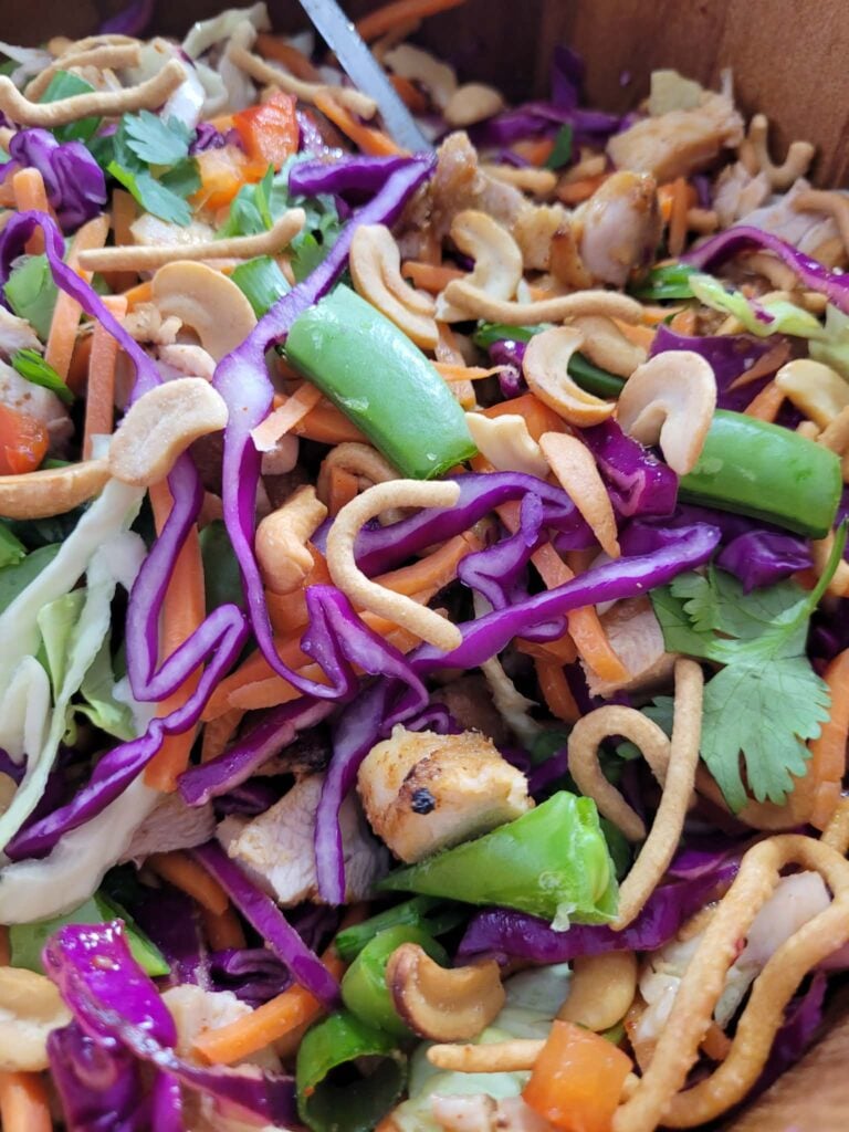 Close-up of sesame ginger chicken salad showing crisp cabbage, colorful vegetables, roasted cashews, and crunchy chow mein noodles