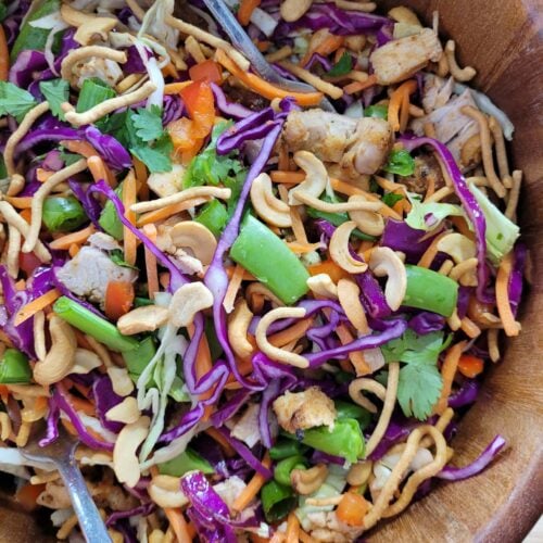 Overhead view of a vibrant crunchy chicken salad with purple cabbage, vegetables, sesame ginger chicken, and cashews