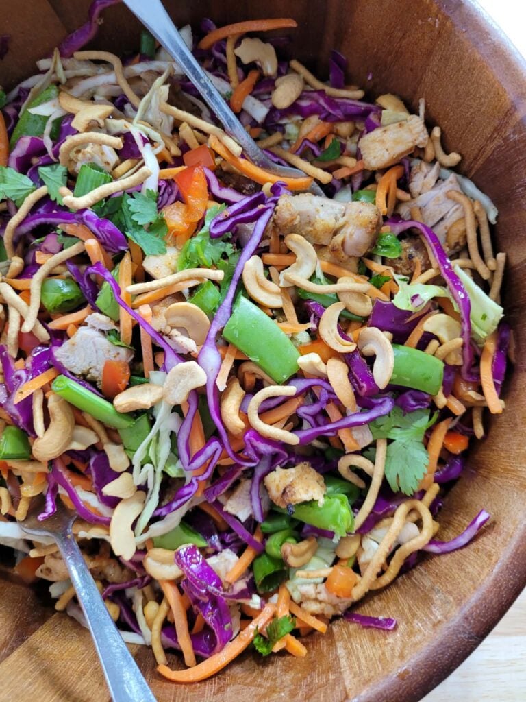 Overhead view of a vibrant crunchy chicken salad with purple cabbage, vegetables, sesame ginger chicken, and cashews