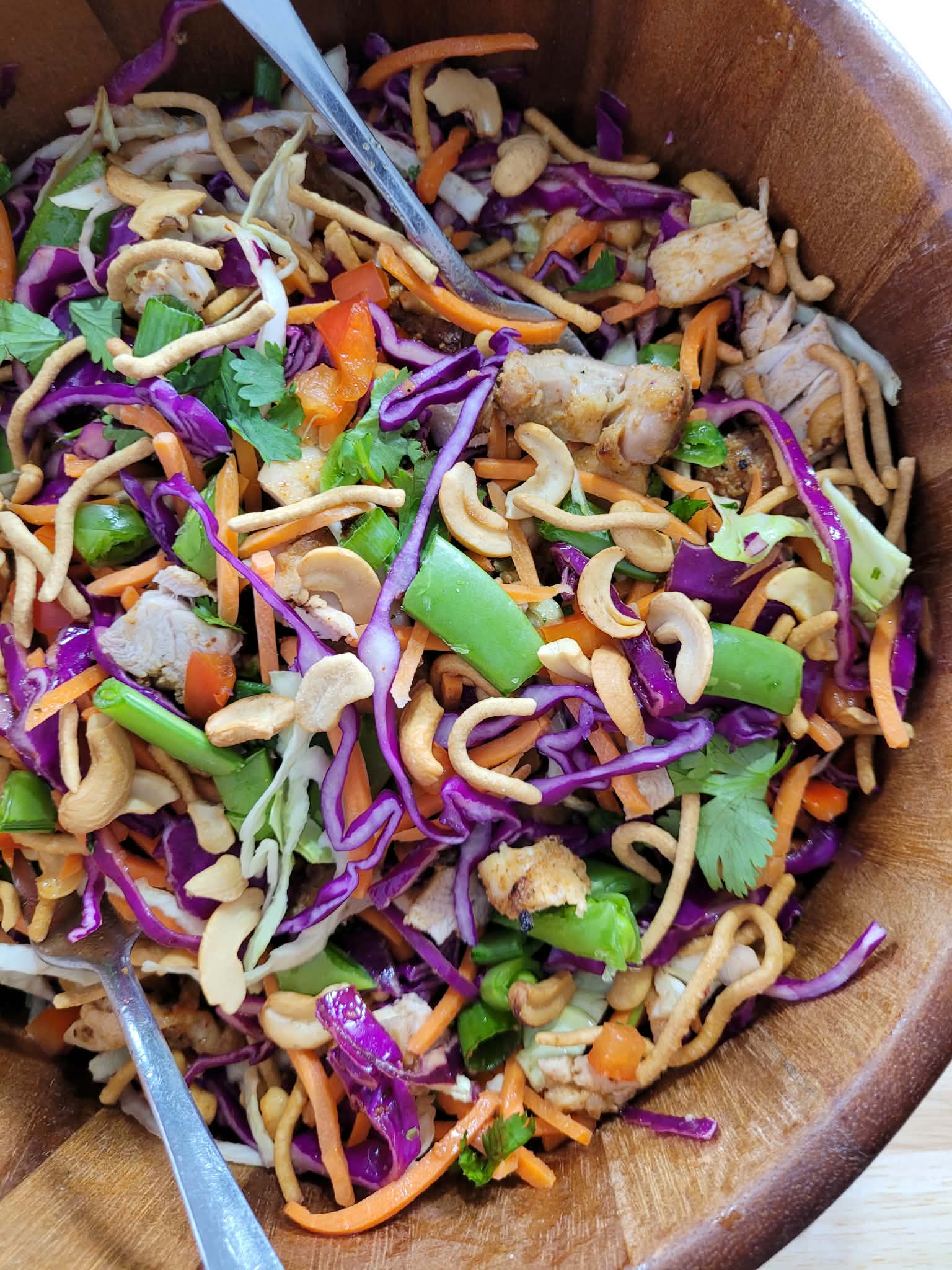 Overhead view of a vibrant crunchy chicken salad with purple cabbage, vegetables, sesame ginger chicken, and cashews