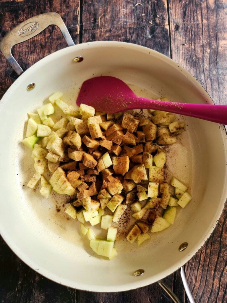 Diced apples cooking with butter, brown sugar, and cinnamon in a skillet